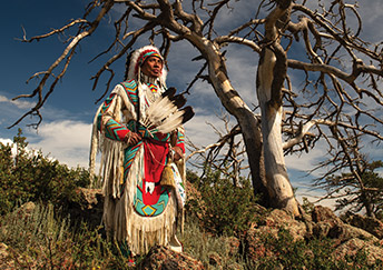 Native American man in traditional clothing under a tree