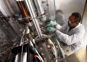 man in lab coat and gloves working with large lab equipment