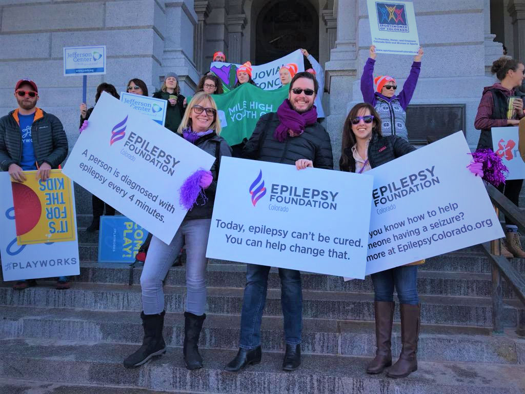 Individuals holding up Epilepsy Foundation signs in front of a building.