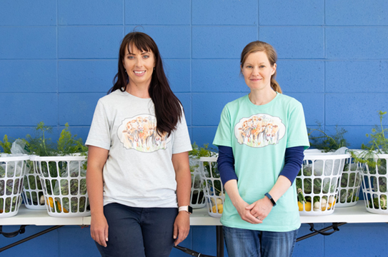 two women standing with baskets full of vegetables