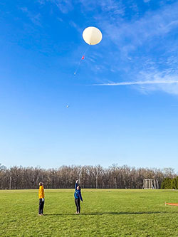 two people watching a large balloon float up into the sky