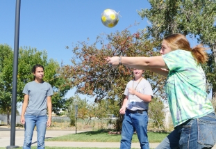 three young people stand in a circle passing a volleyball