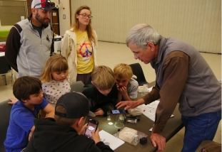a group of children and three adults look at an image of an insect magnified