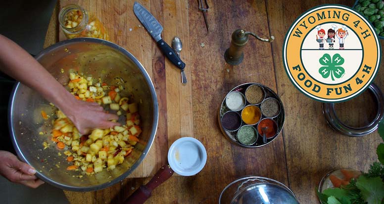 Hands mixing potatoes in a bowl on a table, surrounded by spices