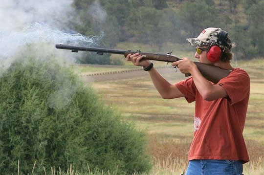 Young man in red t-shirt learning to shoot a shotgun.
