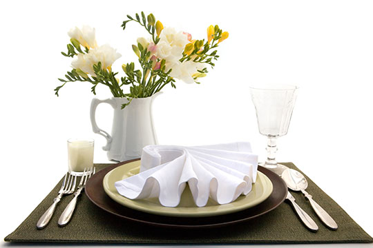 single white and brown place setting with silver utensils on a brown placemat