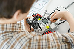 boy in plaid shirt programming Lego robot vehicle