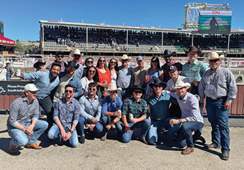 group of people posing with rodeo grounds behind them