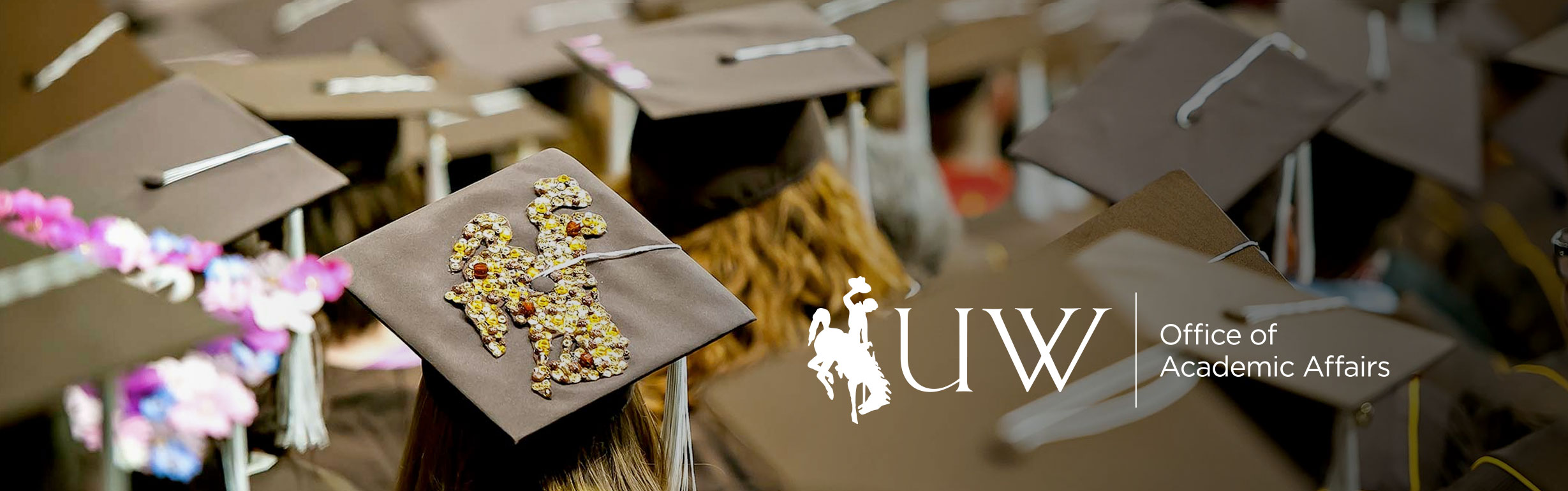 Student at graduation wearing a decorated mortarboard with Office of Academic Affairs logo