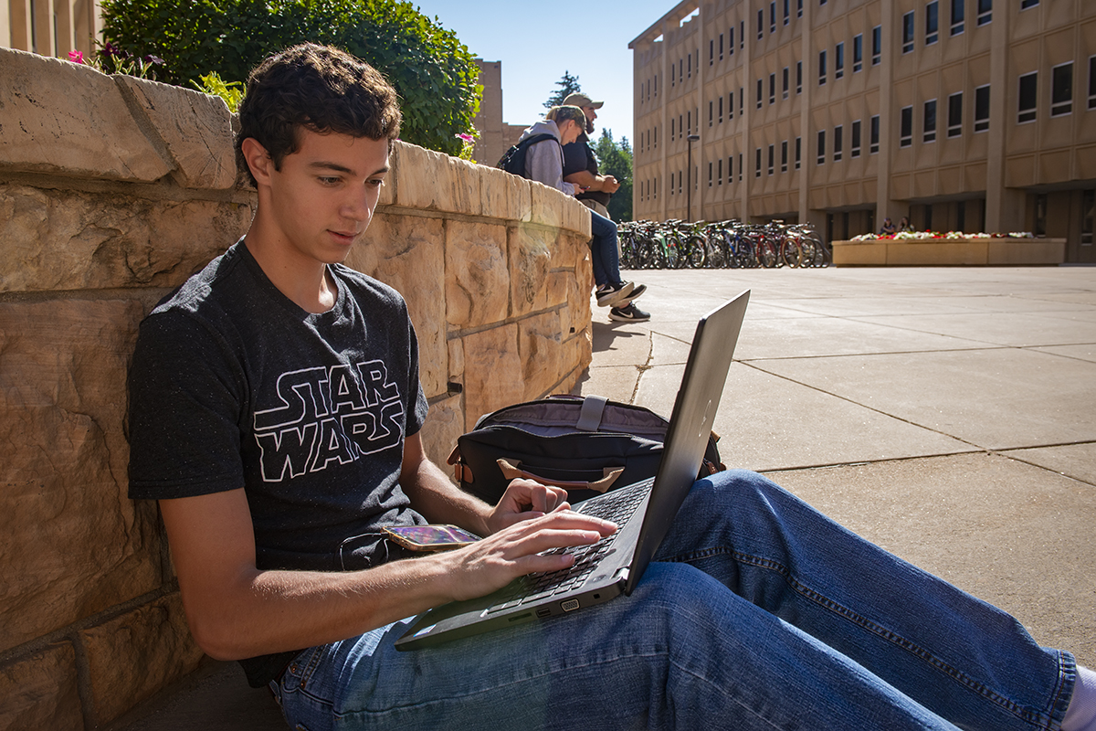 student sitting at his computer outside