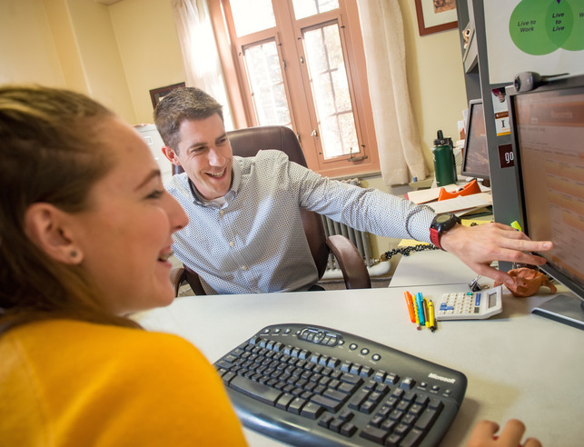 An advisor and student smile as they look over a schedule on a computer screen