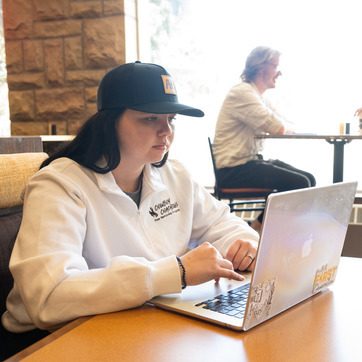 A student sitting at a table in the Rendezvous Cafe in Ross Hall looking at her computer