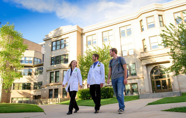 Three health science students walking out of the Health Sciences Building in summer.