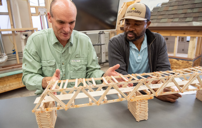 A professor and student building a model bridge using popsicle sticks.