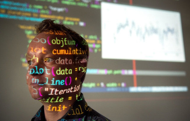 A computing professor standing in front of code that is projected on a wall.