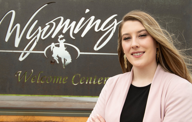 Student standing in front of a State of Wyoming sign at a State of Wyoming Welcome Center in