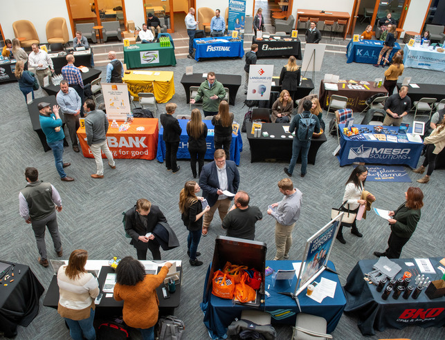 An aerial view of a career fair held in the College of Business building with company booths and students networking