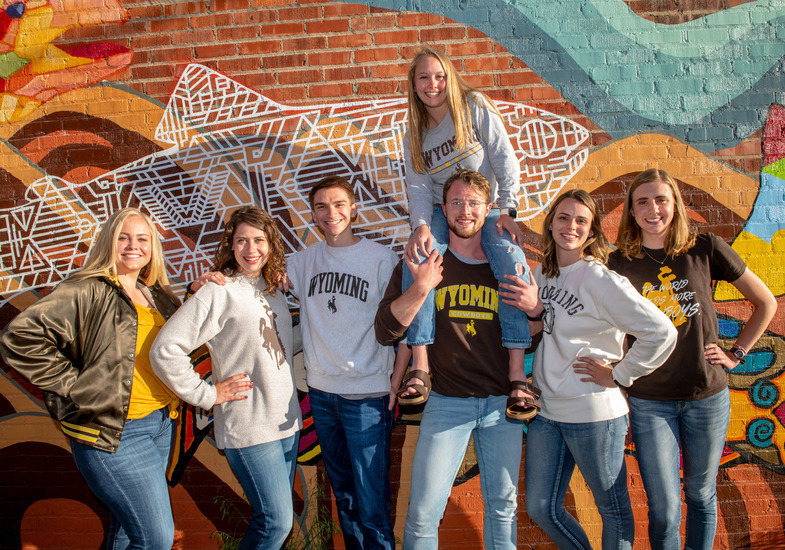 Seven students standing in front of a mural in downtown Laramie