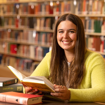 A UW student sits at a table in one of the libraries on campus and smiles with a book in front of them.