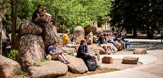 Students sit on a rock together on campus