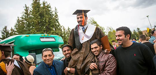 A student sits on the shoulders of another at commencement