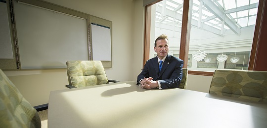 A faculty member sits at a conference room table.
