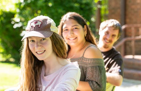 Three students pose together outside in the summer.