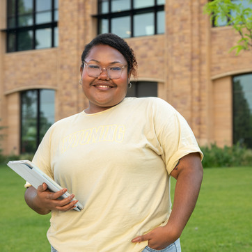 A student proudly stands outside of a UW building with a tablet in hand.