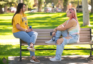 Two students sit on a bench in Prexy’s Pasture and chat between classes.