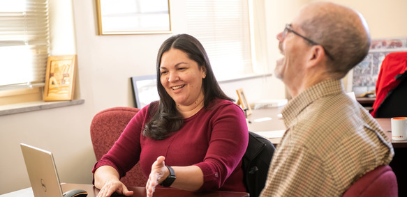 Two UW staff members share a laugh as they work together at a laptop.