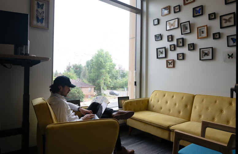 Man sits in a yellow chair working on a laptop computer