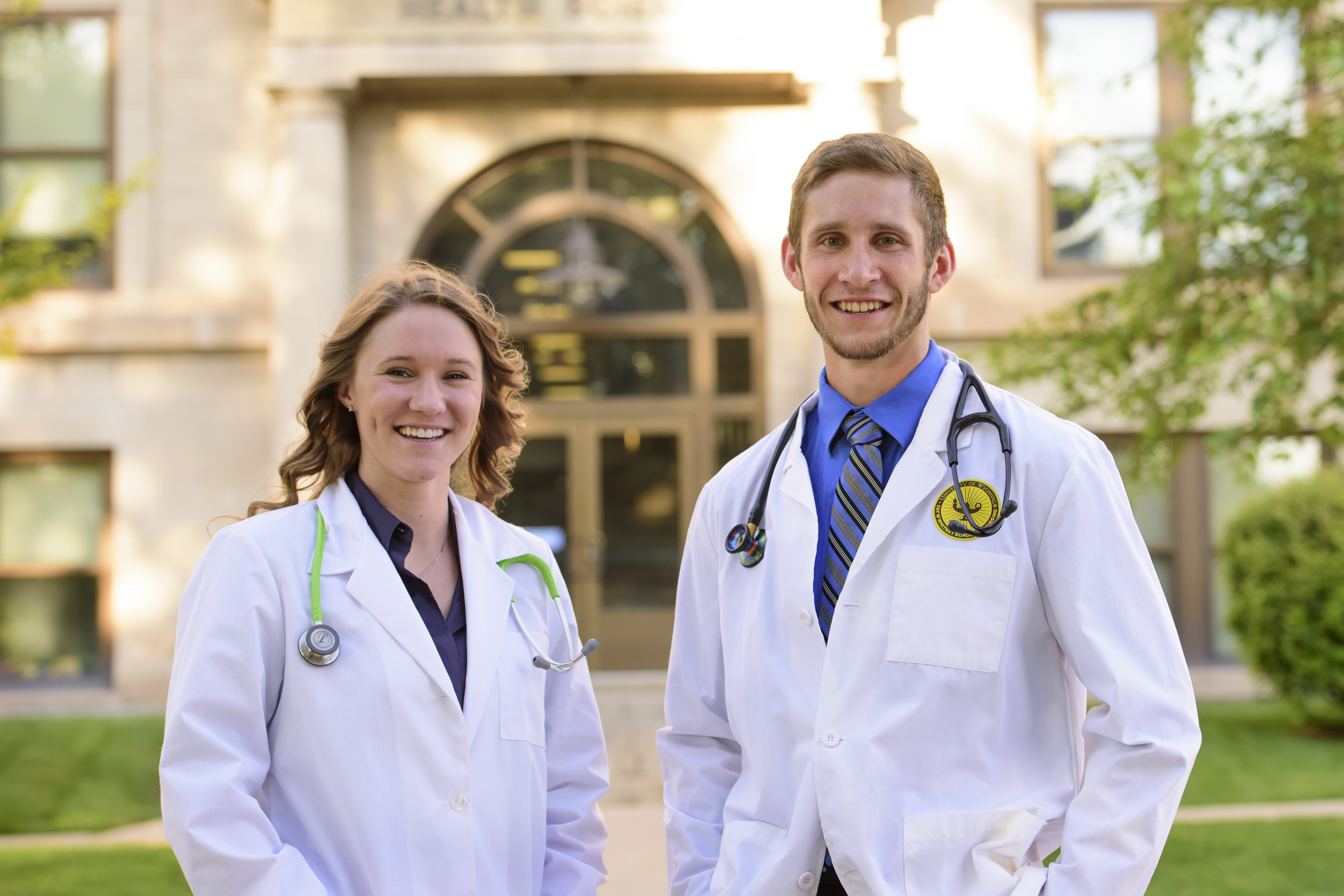 Two smiling students wearing doctor's coats and stethoscopes