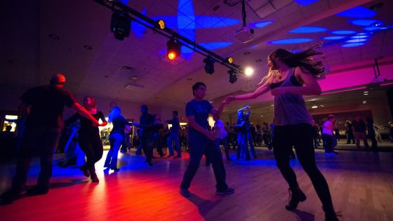 Students swing dancing in dark room with neon lights