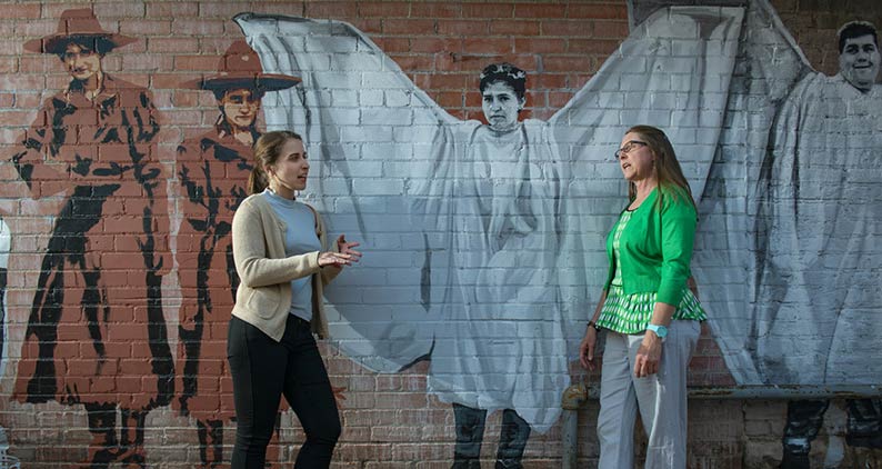 Two students pose in front of a mural in downtown Laramie.