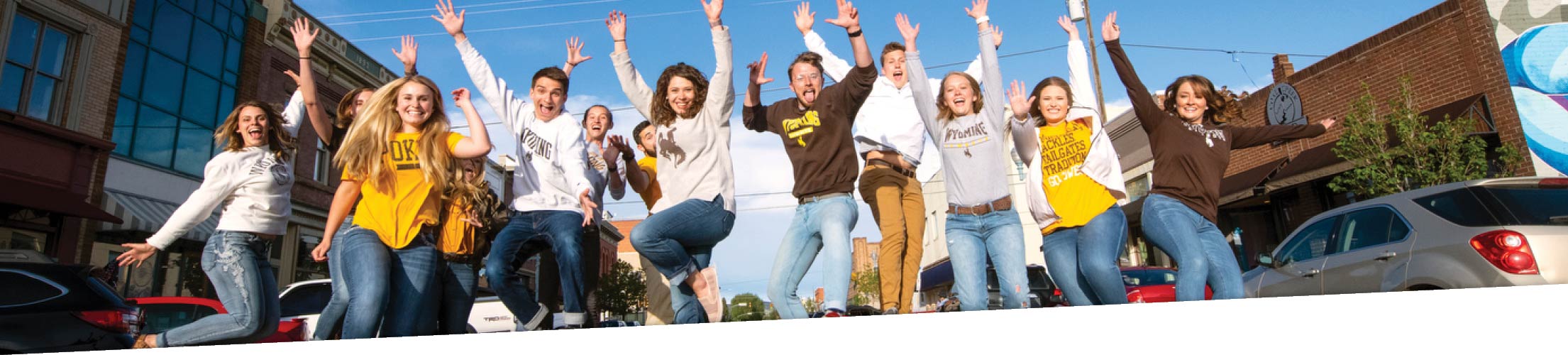 A group of several students jump and smile in a row in downtown Laramie.