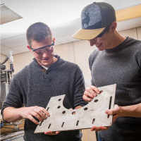 Two students look at a piece of metal together in a machine shop on campus.