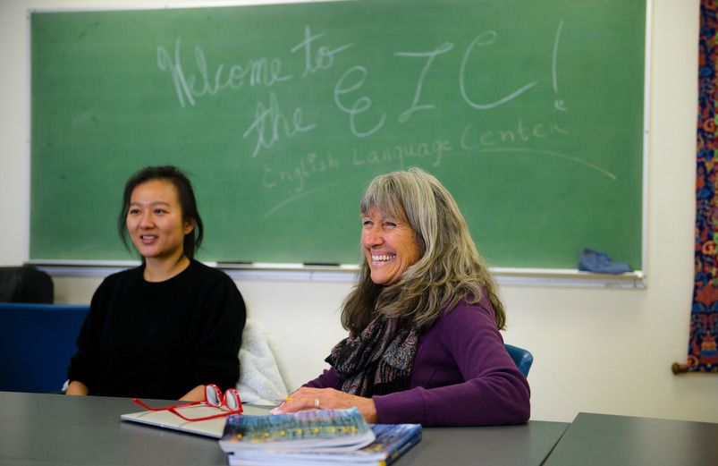 person smiels in font of a chalk board that says "welcome to the English Language Center"