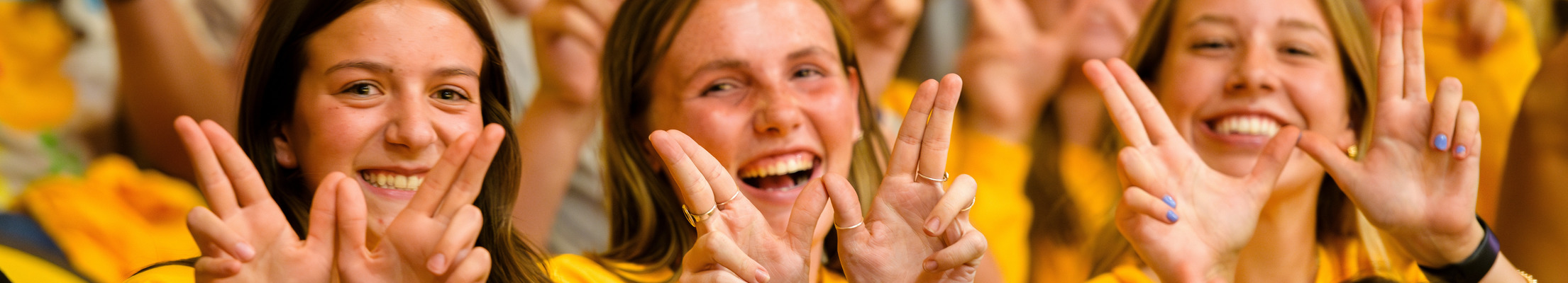 Three students pose with their hands in a "W".