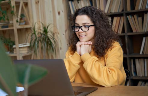 A student sits at a computer in a yellow sweatshirt