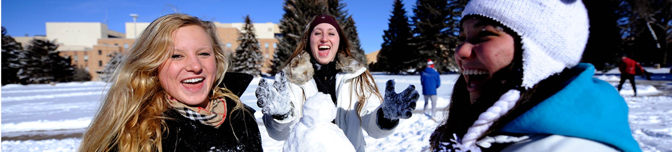 Three students play in the snow together on campus.