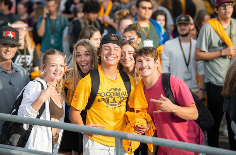 A small group of students wave at the camera at an event.