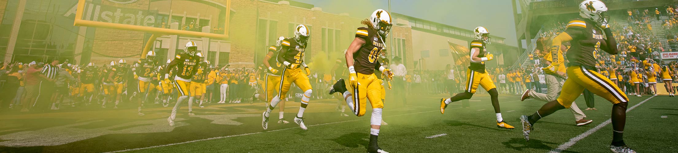 The UW football team charges through a cloud of yellow smoke.