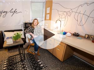 A photo of a student sitting in a chair in their dorm room.