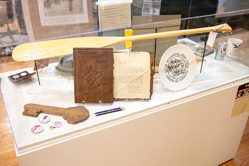 A collection of memorabilia inside an exhibit display case, including plaques, a canoe oar, and a dinner plate