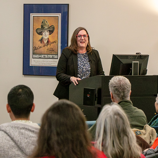 A woman stands behind a lectern and gives a talk to a crowd of people