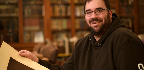 A person smiles at the camera holding a historic portrait from the American Heritage Center.