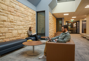Two UW students sit at couches opposite each other as they work independently on their laptops.