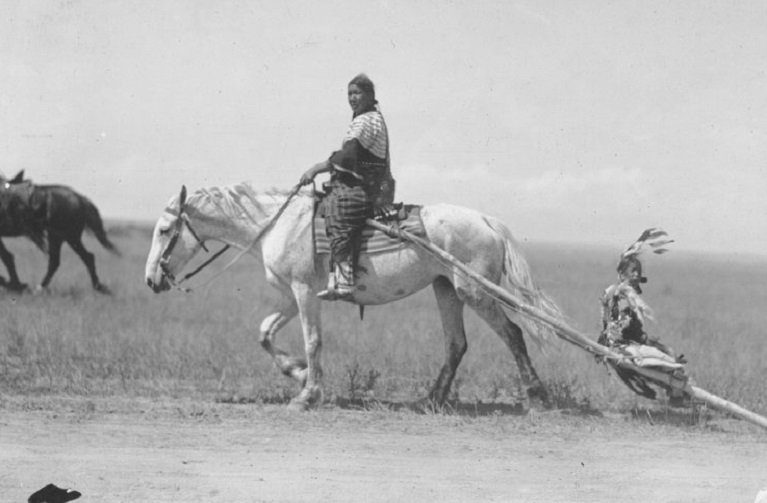 Indiginous woman on horse pulling a child in a sled 