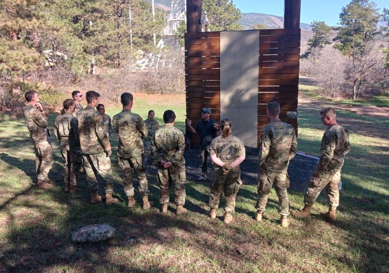 A group of people in military uniform listen to an instructor during a drill.