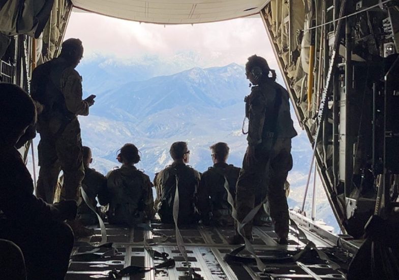 A silhouetted view of an Air Force crew from the back of a C-130 airplane